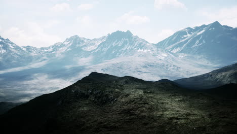 Antena-Sobre-El-Valle-Con-Montañas-Cubiertas-De-Nieve-En-La-Distancia