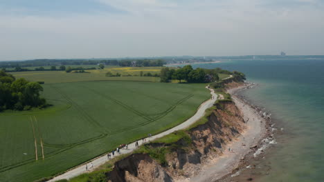 Friedliche-Landschaft-In-Brodten,-Deutschland,-Luftdrohnenansicht-Der-Strandküstenküste-Mit-Blick-Auf-Die-Ostsee-Mit-Weitläufigem-Grünem-Frühlingsfeld,-Dolly-In,-Tag