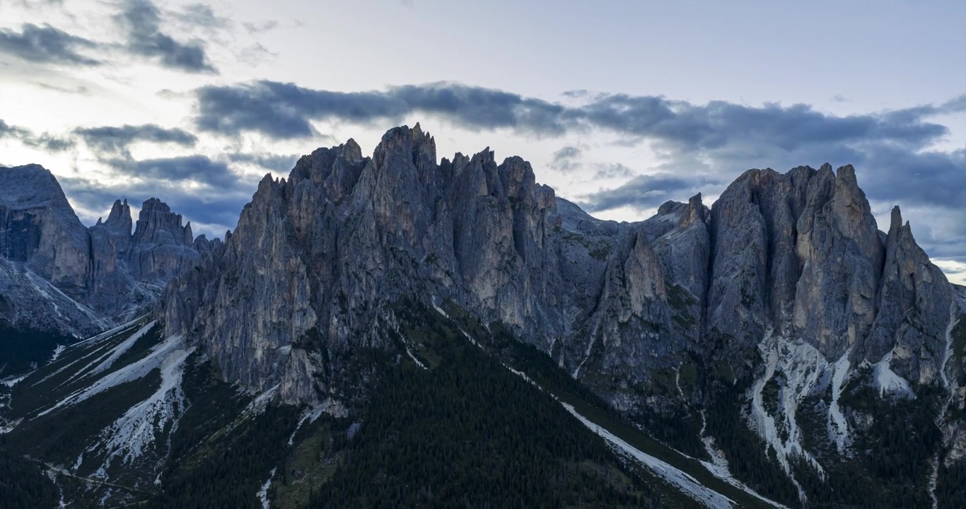 Veduta aerea in hyperlapse delle aspre cime dolomitiche del Catinaccio con nuvole drammatiche e ampie valli alpine