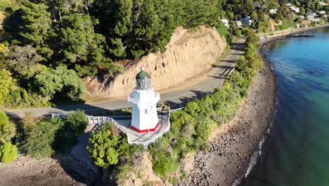 drone footage captures the scenic akaroa lighthouse surrounded by lush greenery and coastal cliffs in bright daylight