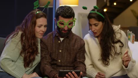 group of friends dressing up at home or in bar celebrating at st patrick's day party looking at photos on phone 1