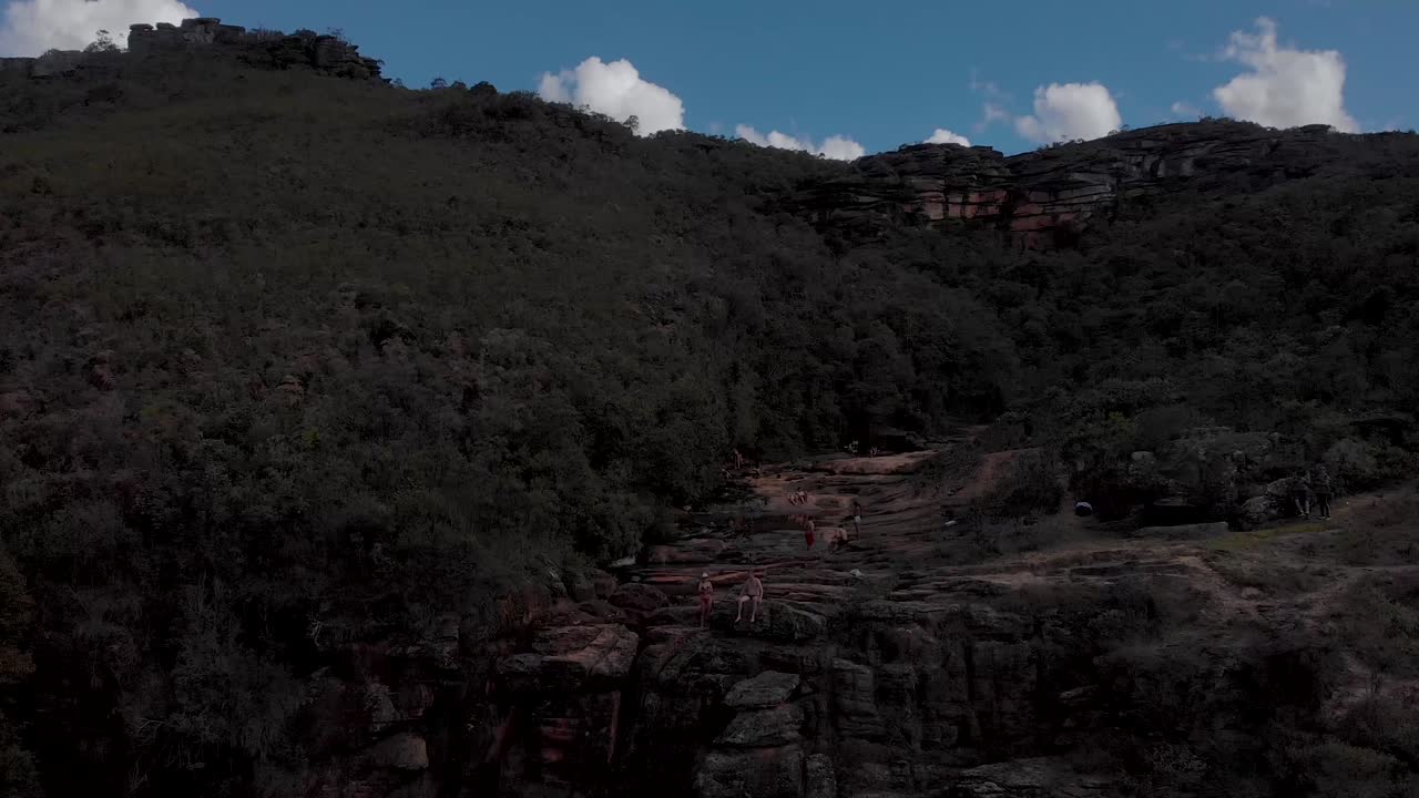 Steady aerial view of a rock plateau river bed with stream of a river cascading and forming ponds with the wider Andorinhas park in the back against a blue sky with clouds near Ouro Preto in Brazil