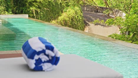 cinematic slider pan of pool towel on sun lounger beside infinity pool