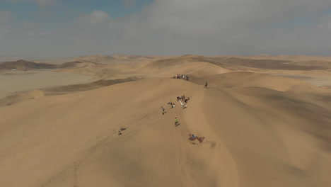 aerial left to right rotation people on to of large dune with sand boards