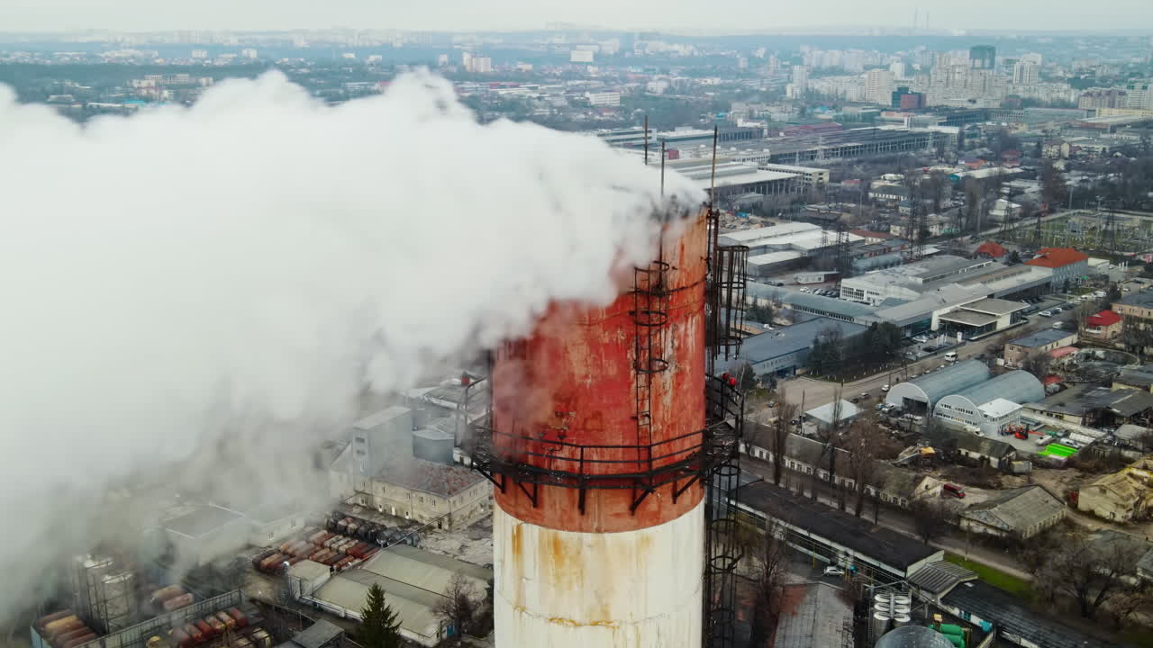 Aerial drone view of thermal station with smoke coming out of the tube. Buildings, roads and bare trees on the background. Cloudy weather. Chisinau, Moldova