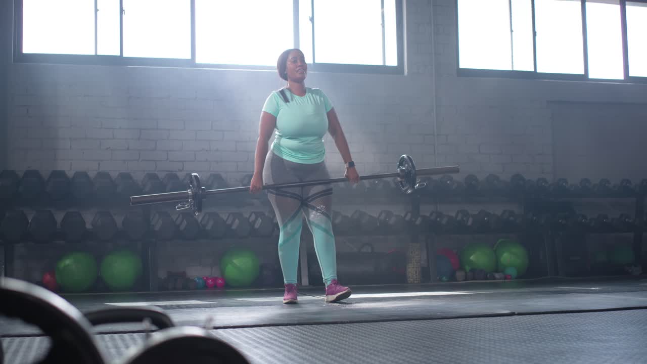 Donna afroamericana che esegue ripetizioni di stacco con bilanciere in palestra dopo aver sistemato i piedi per la forza
