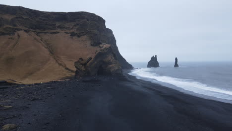 pilar de basalto y playa de arena negra en la toma aérea de la playa de reynisfjara, islandia