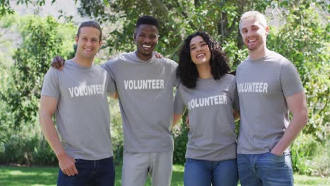 portrait of smiling, diverse group of happy friends in volunteer t shirts embracing outdoors