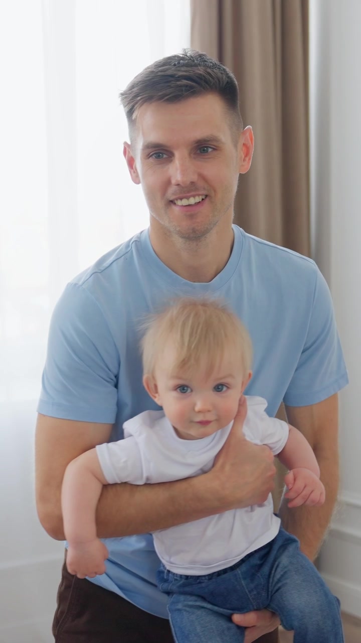 Padre felice che tiene in braccio il suo bambino e sorride alla macchina fotografica