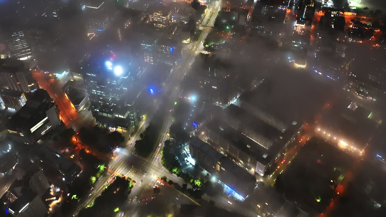 A breathtaking drone view over Cape Town at night, where glowing city lights pierce through drifting mist, revealing bustling streets and modern buildings below