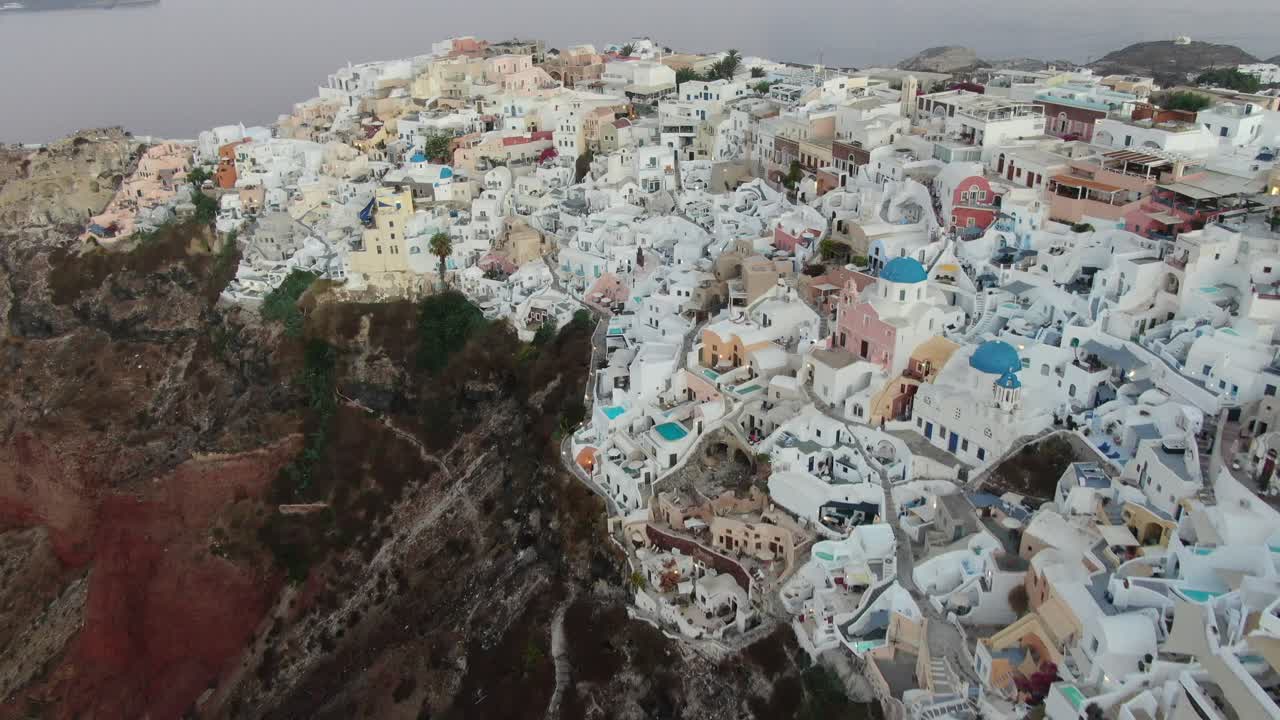 vista de avión no tripulado en grecia volando sobre santorini con la ciudad de oia casas blancas y techos azules en un acantilado junto al mar mediterráneo al amanecer
