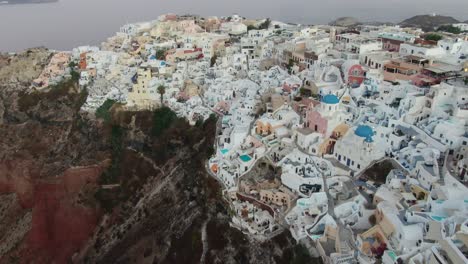 drone view in greece flying over santorini with oia town white houses and blue roofs on a cliff next to the mediterranean sea at sunrise