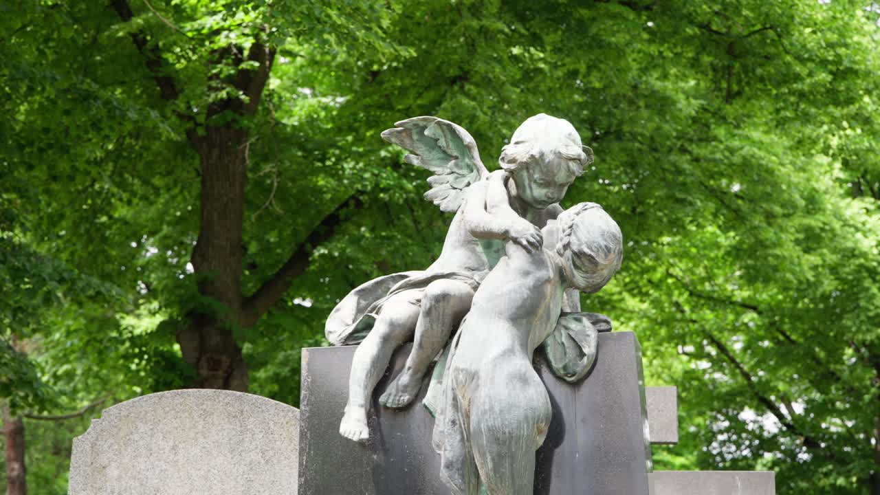 Panoramica sul cimitero Zentralfriedhof attraverso lapidi e statue di angeli tra alberi verdi e lussureggianti, scultura commemorativa storica a Vienna, Austria. Atmosfera estiva calma e riflessiva