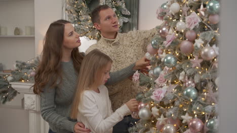 madre, padre y niña decoran el árbol de navidad con bolas y adornos