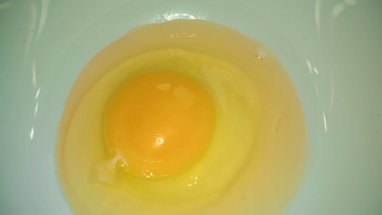 割れた ⁇ 卵が白い鉢に落ちて食事のマクロを調理する
