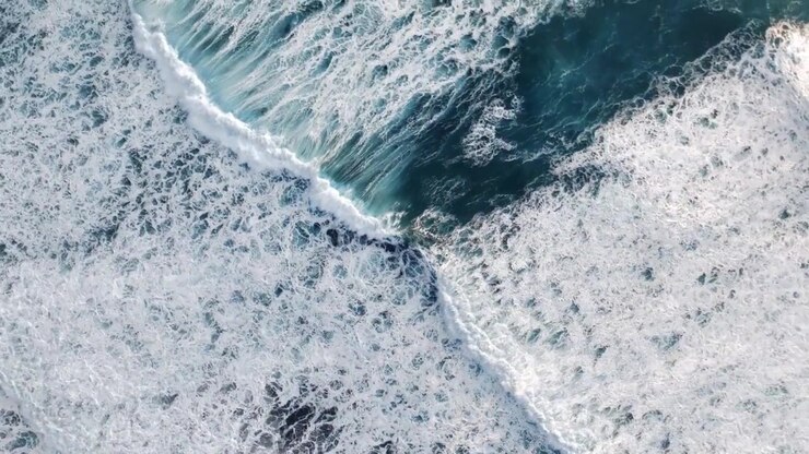 Top down aerial slow motion of turbulent North Atlantic waves generating dense marine foam and ocean turbulence near the rugged volcanic coastline of the Faroe Islands, Kingdom of Denmark.