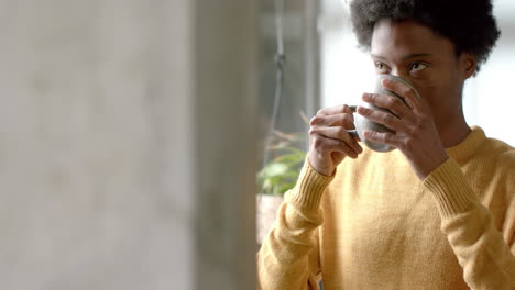 african american man drinking coffee and looking through window at home, slow motion, copy space