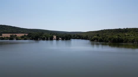 Rising-aerial-of-pond-surrounded-by-trees,-hills,-and-farmland,-Slovakia-country