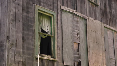 wind blows ripped curtain of broken wooden window, termite infested home, boarded up door