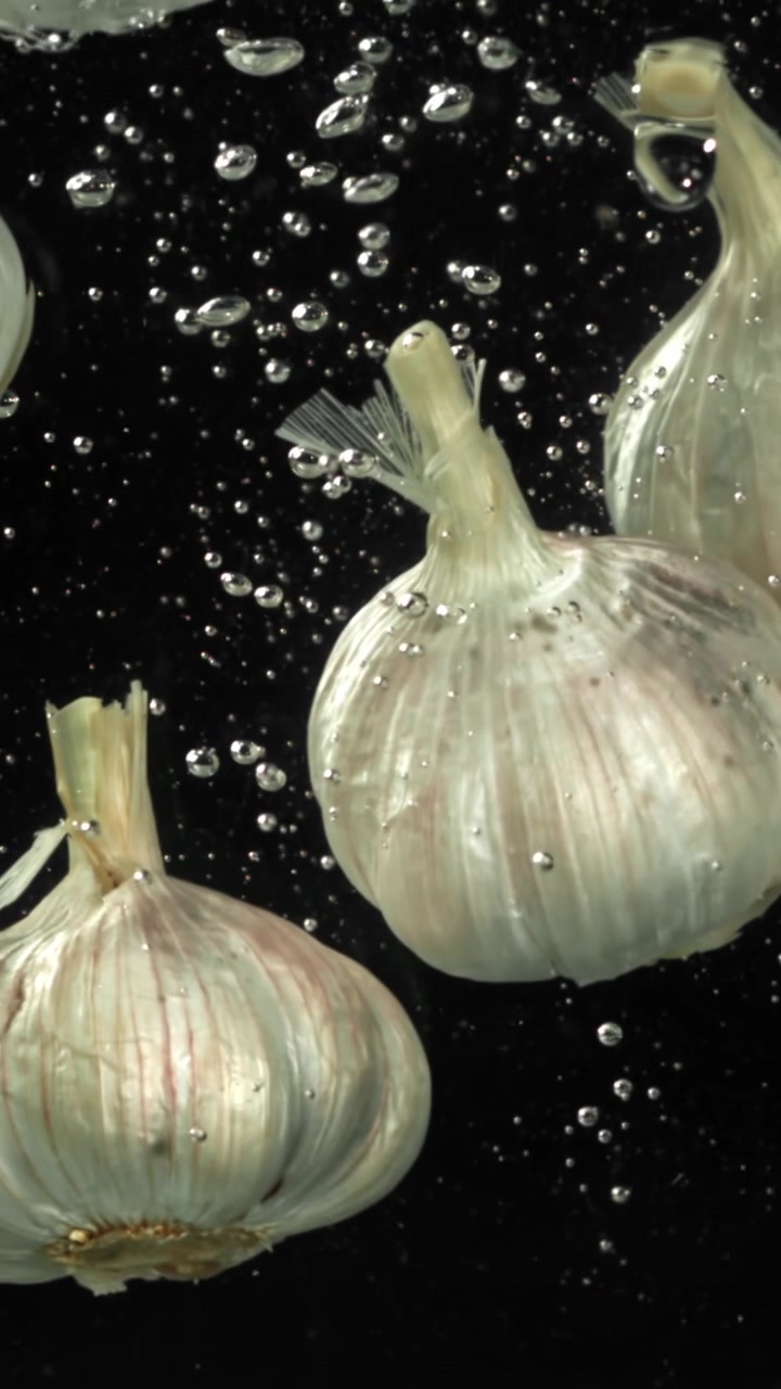 Bulbi d'aglio freschi che galleggiano nell'acqua con bolle su sfondo nero