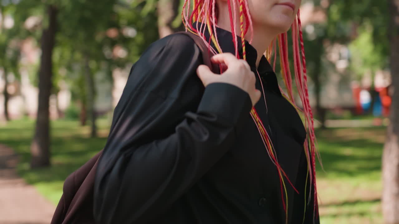 paseo juvenil al aire libre, mujer joven con mochila disfrutando de un día soleado y luminoso al aire libre, adolescente caucásica paseando por un parque con un colorido pelo trenzado y actitud alegre durante el verano