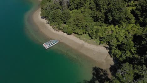 Boat-parked-on-beach-in-Marlborough-Sounds,-New-Zealand-with-crystal-clear-blue-water-and-native-forrest---Aerial-Drone