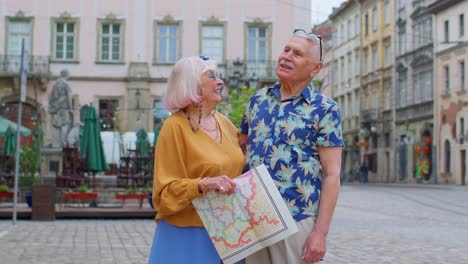 Ancianos-Turistas-Con-Estilo-Hombre-Mujer-Disfrutando-De-Una-Conversación-En-La-Calle,-Sosteniendo-Un-Mapa-De-Papel-En-El-Casco-Antiguo