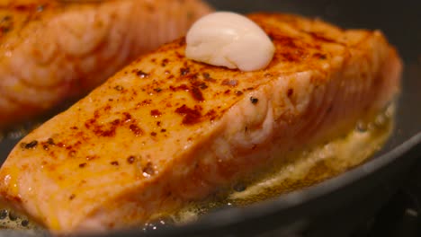 close up of salmon fish fillet cooking in frying pan with oil and butter with garlic resting on top for flavour