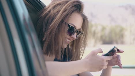 chica agradable mira el teléfono sentada en el coche en el césped en cámara lenta