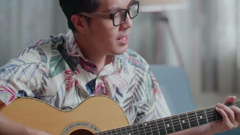 primer plano de un compositor asiático con un cuaderno en la mesa cantando y tocando la guitarra en casa