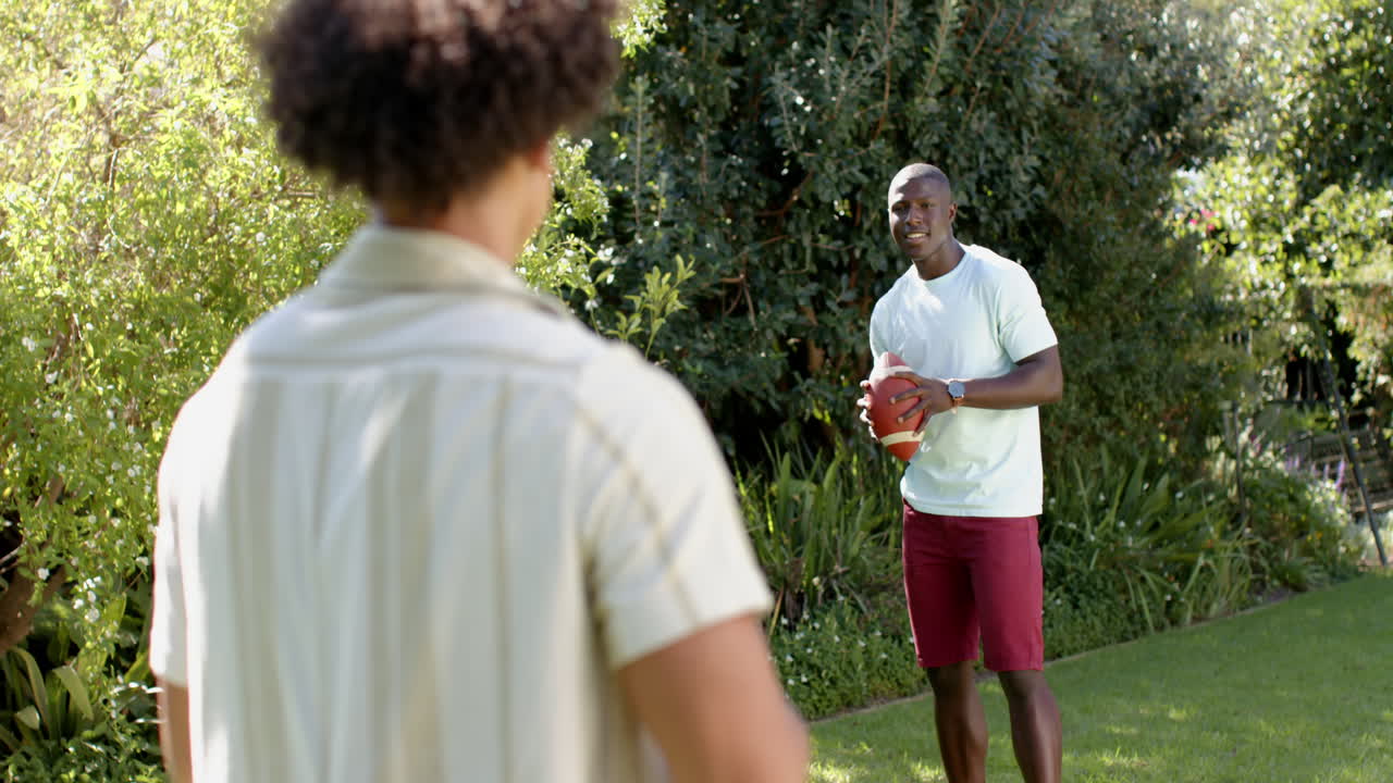 Playing catch with football, two multiracial male friends enjoying outdoor activity together