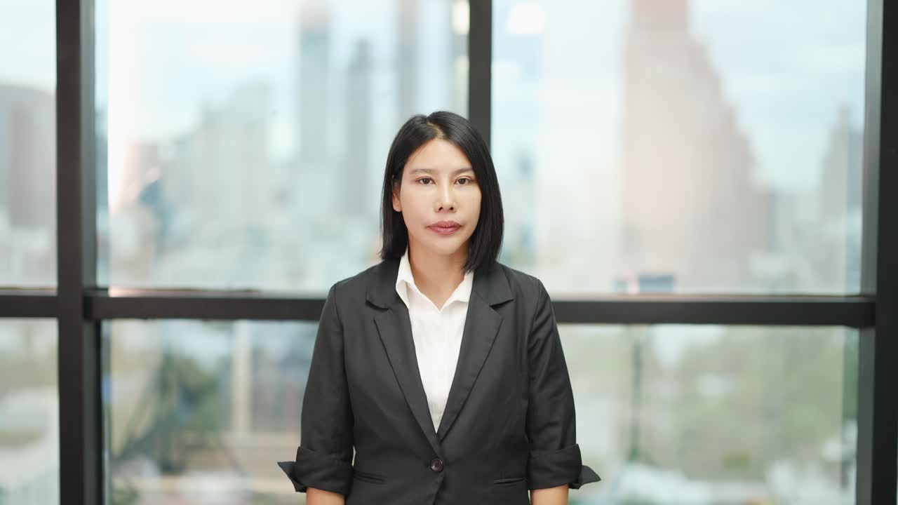 Asian businesswoman in suit raises index finger, expressing disapproval, in bright office setting