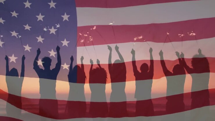 Bandiera americana che sventola sullo sfondo di un gruppo di amici visti di spalle che si divertono con delle stelline in spiaggia.