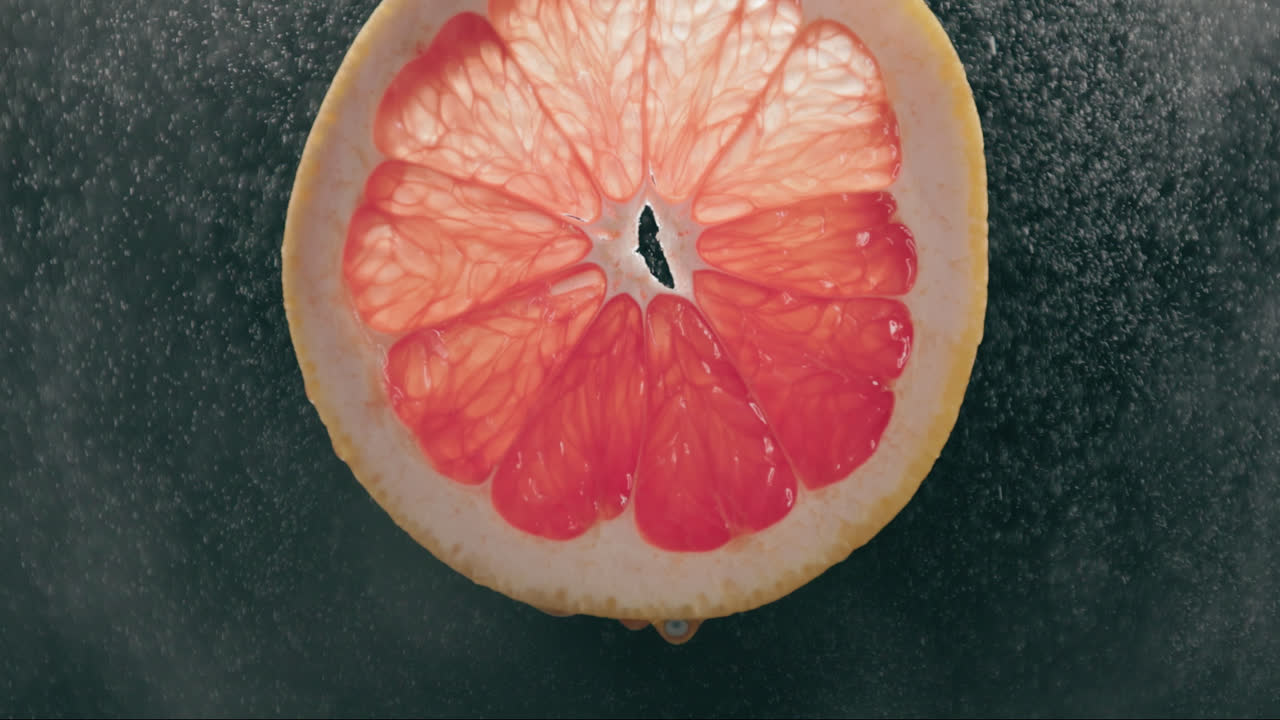 Fresh Grapefruit Slice Splashed by Strong Water Droplet Mist in Slow Motion with Backlit Black Background
