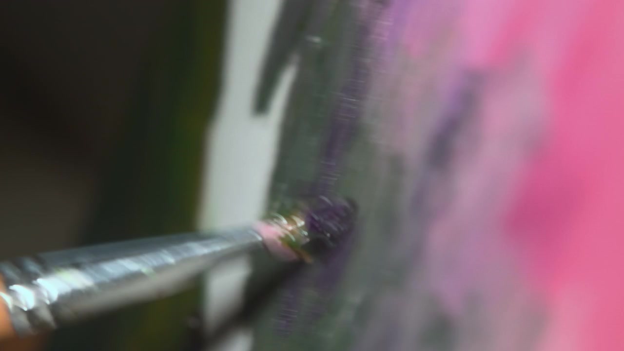 Primo piano di un pennello che stende pittura rosa brillante su una superficie verticale texturizzata con una profondità di campo ridotta, uno sfondo sfocato e morbido e un colore intenso.