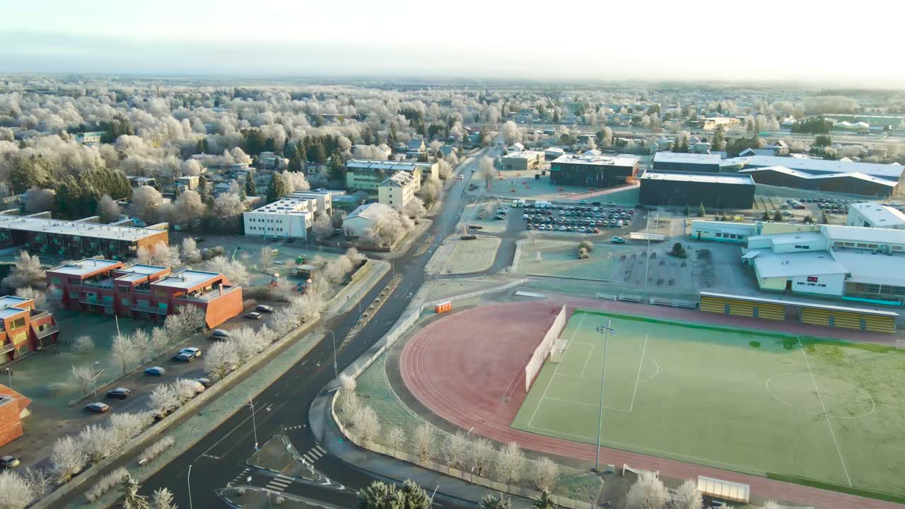 Volo aereo in avanti su una città suburbana gelata all'alba di inizio inverno con stadio di calcio, appartamenti e foresta che si estende fino all'orizzonte.
