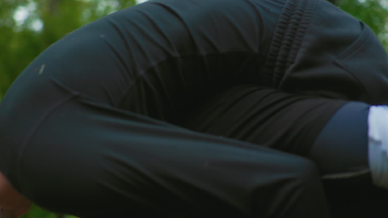 man pinned on park pavement during closeup grappling drill, opponent applies tight grip around legs and torso, training partners test submission and escape techniques, raw contact and focused effort