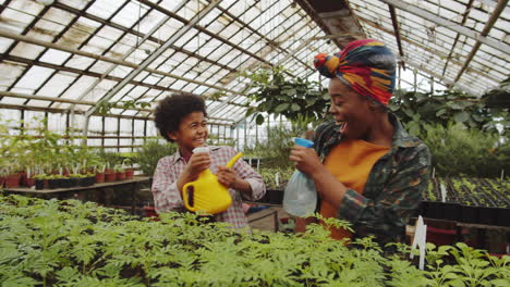 african american mother and son playing water fight in greenhouse