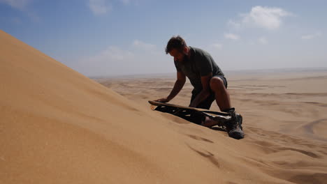 guy on sandy dune waxing sand board