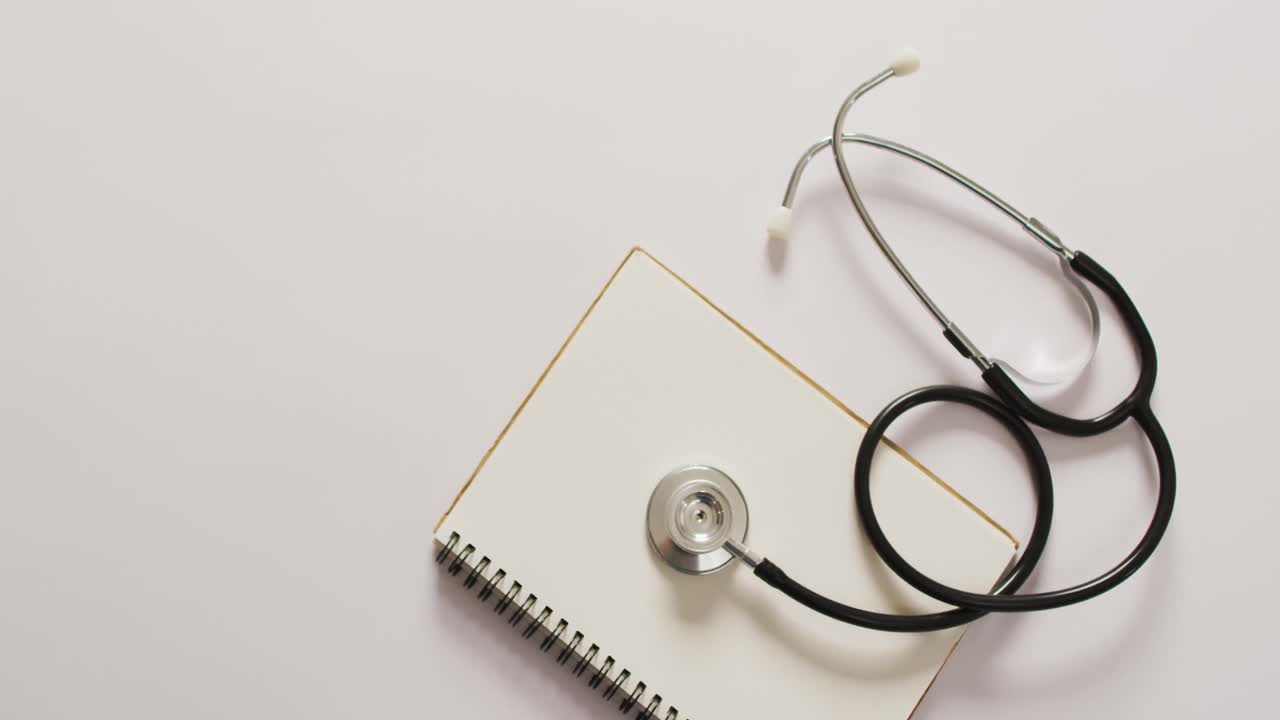 Video of close up of stethoscope with notebook on pink background