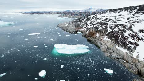 Rocky-coast-of-Greenland-and-floating-iceberg,-aerial-view