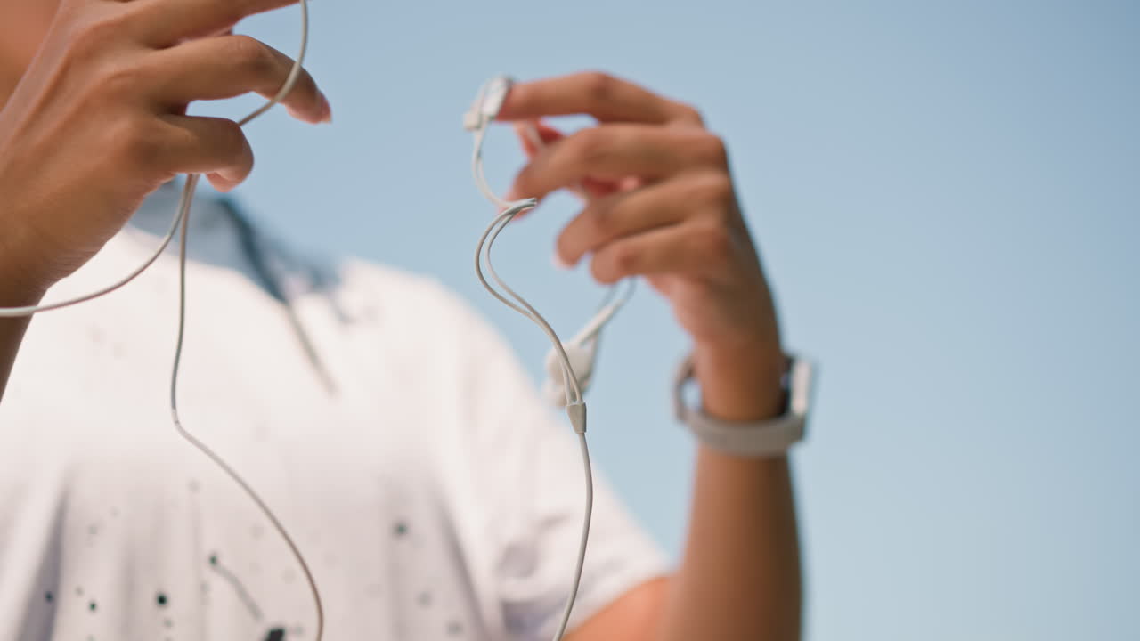 Preparing headphones in morning light, Meticulously arranging audio equipment beneath clear daytime sky, Gentle and deliberate motions of hands organizing music gear before traveling begins