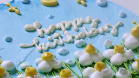 zooming out of a blue birthday cake, covered in blue frosting and decorated with white, yellow-tipped flowers