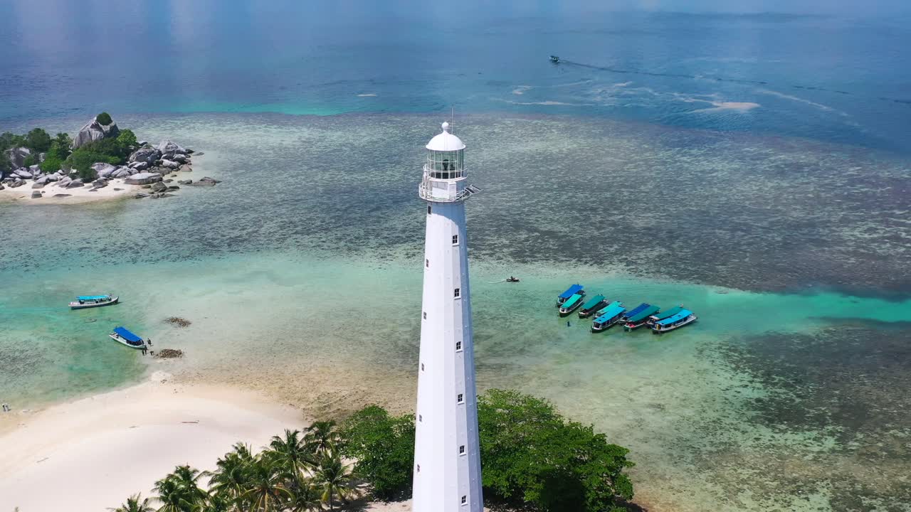 zoom aéreo fuera del faro blanco en la isla lengkuas con barcos turísticos anclados en aguas tropicales de belitung