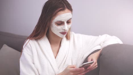 Woman-with-cosmetics-mask-relaxing-on-sofa-and-use-of-mobile-phone