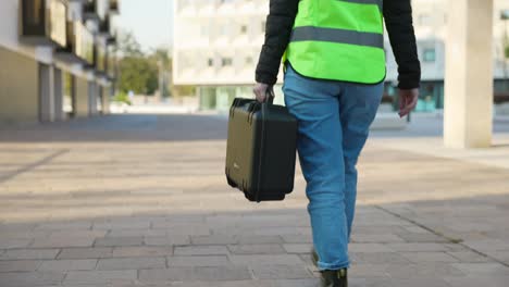 female engineer with high visibility safety vest walks downtown holding drone case