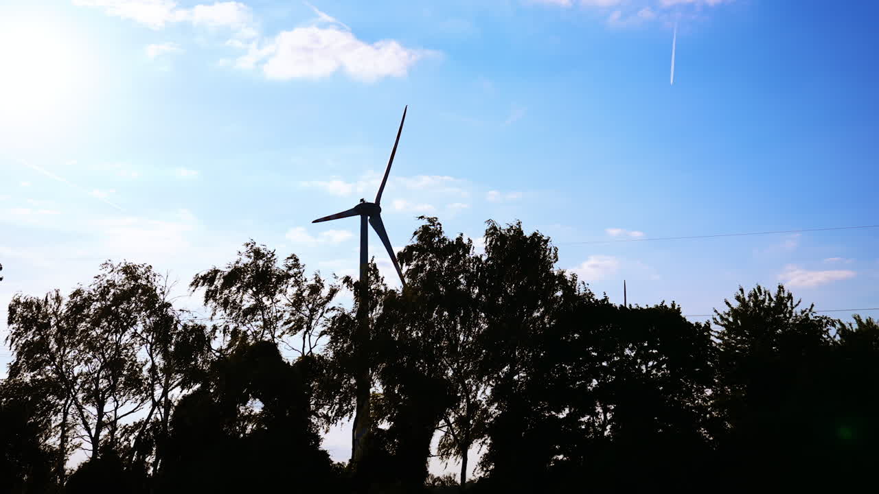 Dark silhouette of the trees waving in the wind. Rotating wind turbines are near the trees