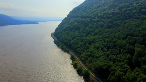 Aerial-drone-footage-of-freight-train-tracks-along-the-Hudson-River-in-New-York's-Hudson-Valley-during-early-autumn-with-mountains-and-a-river-and-forests