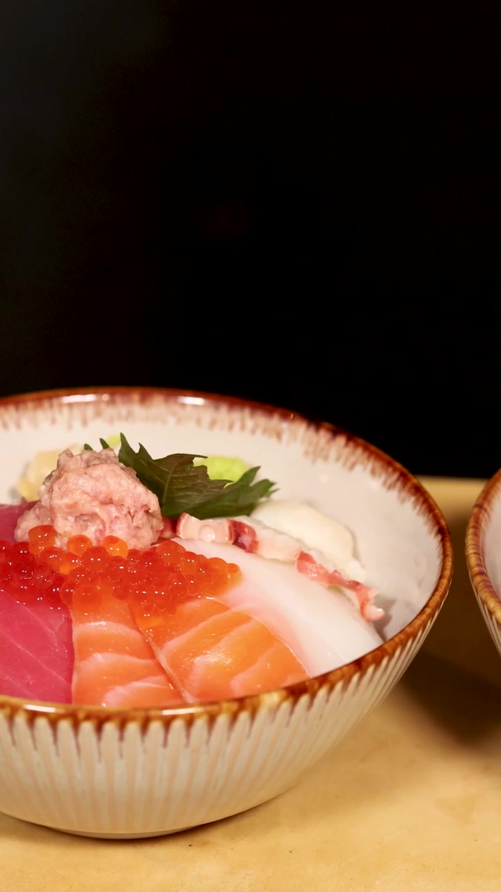 Uno chef usa le pinzette per disporre zenzero e frutti di mare in una colorata ciotola chirashi.