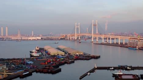 Ein-Geschäftiger-Hafen-Mit-Einer-Markanten-Brücke-Bei-Sonnenuntergang,-Lebhaftes-Hafengeschehen,-Luftaufnahme